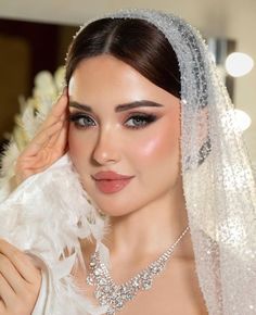 a woman in a wedding dress with a veil on her head and feathers around her neck