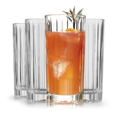 an orange drink in a tall glass next to two glasses with ice and garnishes