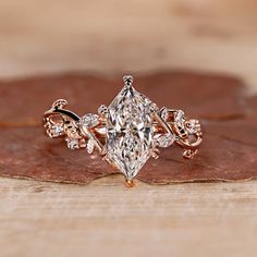 a close up of a diamond ring on top of a wooden surface with leaves in the background