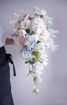 a woman holding a bouquet of white and blue flowers with greenery on the side