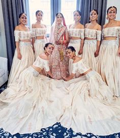 a group of women standing next to each other in front of a window wearing white dresses