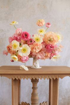 a vase filled with lots of pink and yellow flowers on top of a wooden table