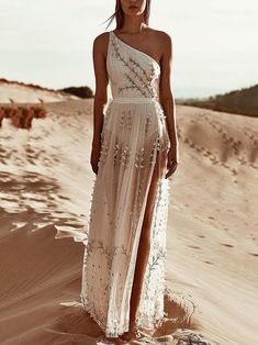 a woman standing in the sand wearing a white dress with flowers on it's side