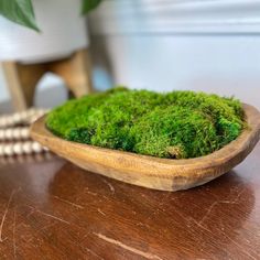 a wooden bowl filled with green moss on top of a table