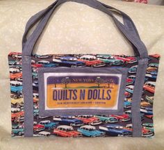 a bag that is sitting on top of a couch next to a pillow with the words quilts n dolls printed on it