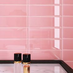 two bottles sitting on top of a counter in front of a pink tile backsplash