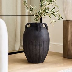 a black vase sitting on top of a wooden table next to a mirror and plant