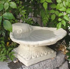 a birdbath sitting on top of a stone wall next to flowers and greenery