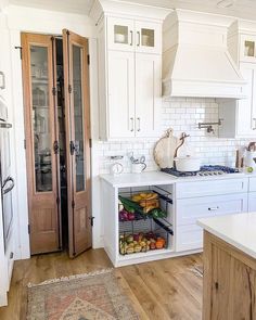 a kitchen with white cabinets and wooden floors, an area rug is on the floor