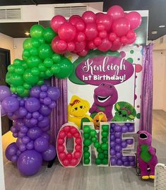 the balloon arch is decorated with purple, green and pink balloons that spell out one