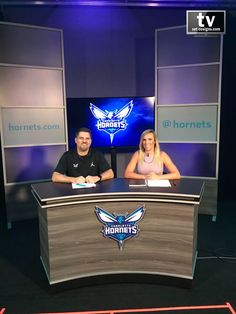 two people sitting at a desk in front of a tv screen with the hornet's logo on it