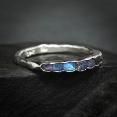 "Raw Uncut Rainbow Moonstone Band Ring // Silver Gold Raw Rough Uncut Organic Rustic Blue Flash Unique Rainbow Moonstone Wedding Band Ring This listing is for one raw natural Rainbow Moonstone band stone ring. Pictured ring is in sterling silver with dark base. DETAILS:  Stone: natural raw Rainbow Moonstone, dark metal base Metal:  - 925 silver  - 925 oxidise black (will start wearing lighter/off immediately) - 14k yellow, rose and white gold - 18k yellow gold Band width: approx. 2x1mm, hammered Fusion Style Moonstone Gemstone Ring For Anniversary, Fusion Style Anniversary Moonstone Gemstone Ring, Anniversary Fusion Style Moonstone Gemstone Ring, Anniversary Fusion Style Moonstone Ring, Blue Moonstone Promise Ring, Wedding Sapphire Ring With Stones In Silver, Fusion Style Wedding Ring With Birthstone, Wedding Sapphire Ring In Silver, Unique Stackable Moonstone Ring For Wedding