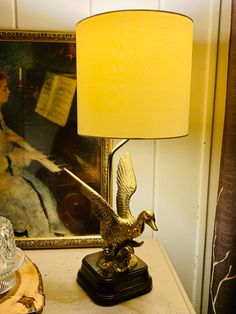 a lamp sitting on top of a table next to a painting and a bird figurine