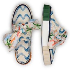 a pair of white shoes with blue and orange flowers tied to the top of them