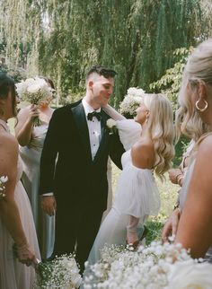 a man in a tuxedo standing next to two bridesmaids and holding bouquets