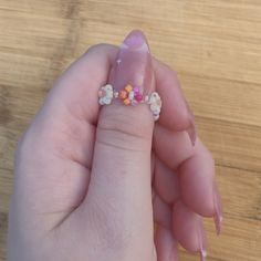 a woman's hand holding a pink ring with flowers on it and two fingers