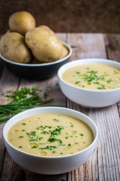 two bowls filled with soup sitting on top of a wooden table next to potatoes and green onions