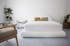 a white bed sitting in the middle of a room next to a chair and potted plant