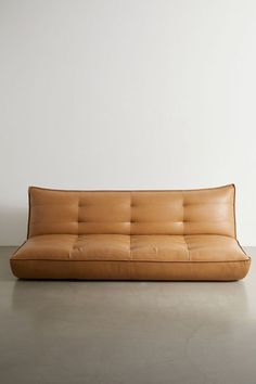 a brown leather couch sitting on top of a cement floor next to a white wall