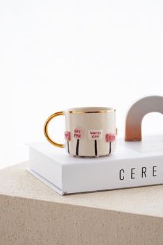 a white and gold coffee cup sitting on top of a book next to a ring