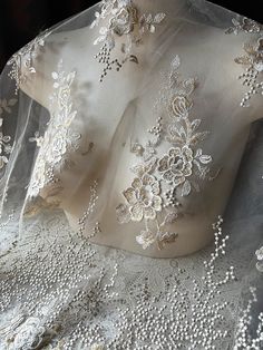 the back of a wedding dress with white flowers and pearls on it's lace