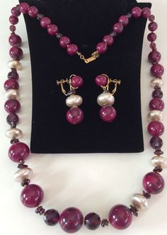 Here is a rare and absolutely ravishing vintage jewelry parure by highly coveted designer Miriam Haskell. It consists of a beautiful decadent necklace and matching dangly earrings that are exquisitely crafted with big glossy bakelite beads in a rich marbled maroon shade, lustrous chunky faux baroque pearls, sparkling translucent faceted glass beads in regal purple amethyst tones and glistening natural garnet stones. The necklace beads, pearls and garnet chips are linked in between accents of... Vintage High Luster Jewelry For Anniversary, Vintage Polished Beads Jewelry For Wedding, Vintage Pearl Necklace With Polished Beads For Gifts, Vintage Handmade Pearl Necklace For Formal Occasions, Vintage Purple Round Beads Jewelry, Handmade Vintage Pearl Necklace For Formal Occasions, Vintage Purple Round Bead Jewelry, Miriam Haskell Necklace, Amethyst Art