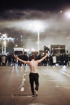 a shirtless man is running in the middle of a street with police trucks behind him