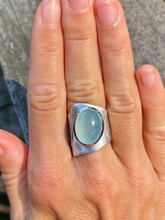 This one is a true eye catcher. Very modern and contemporary adjustable sterling silver ring with perfect diamond aqua chalcedony cabochon. Looks amazing and very hip on when worn. Asymmetrical shape of ring will surely make a statement. The wide band is of free -form adjustable design, very original, yet simple. The band is not only has a free - form wavy contour but also slightly etched to give the band a matte finish to match the chalcedony. Very beautiful, industrial and comfortable to wear Long Silver Ring, Silversmith Jewelry Inspiration, Modern Oval Cabochon Jewelry With Large Stone, Modern Oval Sterling Silver Moonstone Ring, Modern Rings With Large Oval Cabochon Stone, Modern Adjustable Oval Moonstone Ring, Modern Oval Moonstone Ring With Large Stone, Handmade Oval Moonstone Ring In Modern Style, Modern Moonstone Ring With Large Stone