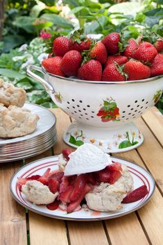 strawberry shortcakes with whipped cream and strawberries in a colander on a table