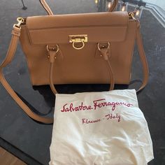 A Salvatore Ferragamo Purse From The Lotty Collection Styled In Pebbled Calfskin Leather With Gold-Tone Hardware And A Fully Lined Interior. This Bag Features 2 Open Pockets With A Flap Secured By Gancio Flip Lock, 1 Interior Zip Pocket And One Front Exterior Zip Pocket. Additional Features Include 2 Rolled Leather Handles With 7.5" Drop. Dimensions 10" Height 13" Wide 5" Deep Bought In Italy New For Work Clothes Accessory But Never Used Because I Prefer Bags With Shoulder Straps Only. Pre-owned Top Handle Bags For Formal Occasions, Pre-owned Elegant Leather Shoulder Bag, Elegant Pre-owned Leather Shoulder Bag, Pre-owned Elegant Top Handle Bag, Elegant Pre-owned Top Handle Bag, Elegant Pre-owned Rectangular Bag, Chic Pre-owned Leather Bag, Salvatore Ferragamo Bags, Work Clothes