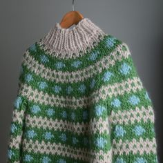 a green and white sweater hanging on a wooden hanger