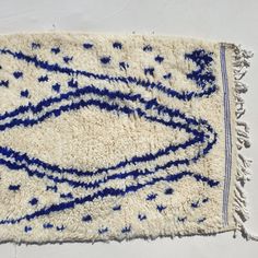 a blue and white area rug with fringes on the bottom, in front of a white wall