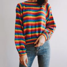 a woman wearing a multicolored sweater and jeans with her hands in her pockets