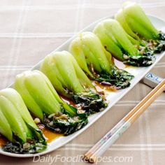 some food is on a plate with chopsticks next to it and there are green vegetables in the middle