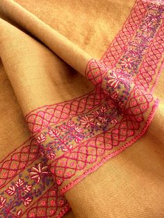 an orange and pink scarf with intricate designs on it's edges, sitting on top of a table