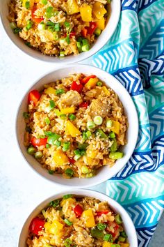 three bowls filled with rice and veggies on top of a blue towel next to a spoon