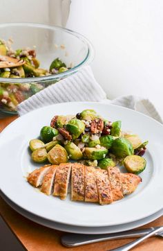 a white plate topped with brussel sprouts next to a bowl of chicken