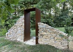 a stone wall with an open door in the middle of it, surrounded by grass and trees