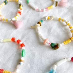 four bracelets with beads and tassels on a white cloth tablecloth,