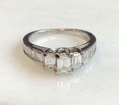 Here is a beautiful 14k white gold emerald cut diamond ring. The center stone is .20ct. with 2 side emerald cut diamonds totaling .30ct. There are also 16 baguettes in the band totaling .56ct. A beauty that will get a lot of compliments! Metal: 14K White Gold Diamonds: 1-Emerald Cut .20cttw, 2-Emerald cut .30cttw, G/H, VS, 16-side stones .56cttw, Weight: 3.8 grans Size: 6.5 SKU# 21SB080619 If you have any questions on this item, please message us! GandDJewelers.etsy.com Please note that all of o Octagon White Gold Diamond Ring With Baguette Diamonds, White Gold Octagon Diamond Ring With Baguettes, White Gold Octagon Diamond Ring With Baguette Diamonds, Fine Jewelry Emerald Cut Diamond Ring With Baguette Diamonds, White Gold Emerald Ring With Baguette Diamonds, Platinum Diamond Ring With Baguette Emerald Cut, White Emerald Cut Platinum Diamond Ring, Platinum Diamond Ring With Emerald Cut And Accents, Emerald Cut Platinum Diamond Ring With Accents