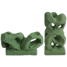 two green sculptures sitting next to each other on top of a white surface and one is made out of cement