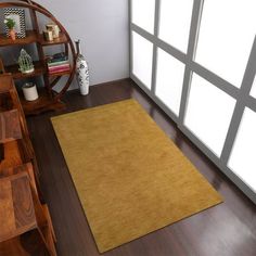 a brown area rug on top of a wooden floor next to a book shelf and window