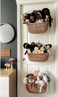 two baskets filled with stuffed animals hanging from the side of a white door next to a dresser