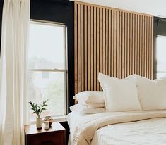 a bed with white sheets and pillows next to two windows in a room that has wooden slats on the walls