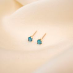 two small blue stones sitting on top of a white cloth next to a pair of earrings