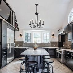 a large kitchen with black cabinets and an island in the middle is lit by two chandeliers