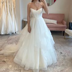 a woman in a white wedding dress taking a selfie with her cell phone while standing in front of a pink couch