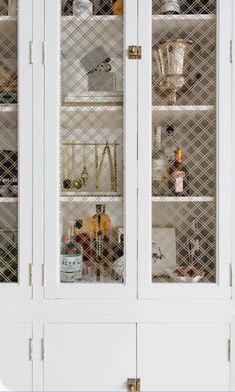 a white cabinet with glass doors and shelves filled with bottles, glasses, and other items