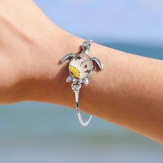 Exquisite and refined, the nautically-inspired Pressed Daisy Sea Turtle Bracelet adds a touch of elegance to any outfit. This unique bracelet is the perfect reminder of warmer weather and happy beach memories for your favorite beach lover.  Details:  Eco-friendly Alloy with Silver Finish Real Daisy in Resin Oval Size: 65mm (length) x 55mm (width) Sunshine on your neck, the ocean in your ears. Discover GoBeachy jewelry - where summer never fades. Dive into sun-kissed sparkle, where quality meets Bohemian Flower Bracelets For Vacation, Ocean-inspired Jewelry With Lobster Clasp For Vacation, Ocean-inspired Jewelry For Vacation With Lobster Clasp, Ocean-inspired Bangle Jewelry For Gifts, Nickel-free Sterling Silver Bracelets For The Beach, Ocean-inspired Silver Bracelets As Gifts, Bohemian Flower Charm Jewelry For Beach, Unique Flower-shaped Beach Jewelry, Unique Flower Jewelry For Beach