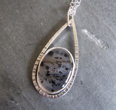 "This pendant features a pretty Montana agate in a unique sterling silver setting. The Montana Agate came from a man in Livingstone, Montana who finds agates along the Yellowstone River, cuts, and polishes them himself. The stone is oval and clear with many dark  spots within.  A typical Montana Agate. I set the stone in a fine and sterling setting.  It resides inside a teardrop shaped hammered frame that I constructed.   The pendant measures approx. 2\" by 7/8\". The sterling chain is 21\" long Silver Agate Oval Cabochon Jewelry, Silver Agate Jewelry Oval Cabochon, Silver Agate Jewelry With Oval Cabochon, Silver Agate Jewelry In Oval Cabochon Shape, Silver Agate Teardrop Pendant Jewelry, Yellowstone River, Metalsmithing Jewelry, Livingstone, Montana Agate